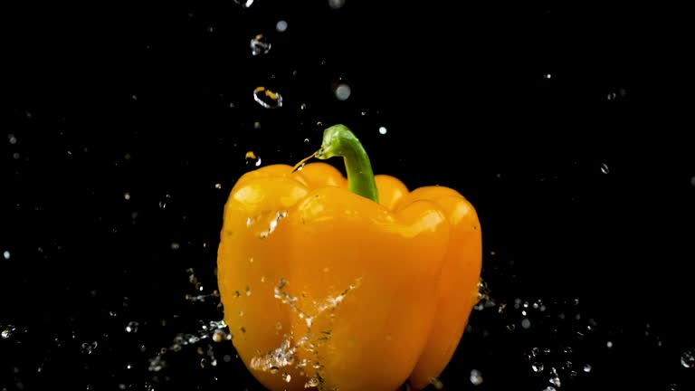 A yellow bell pepper spins as water droplets splash against it, set against a black background, representing the concept of freshness and vitality. HDR, 4K.