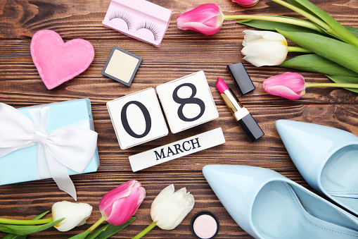 Tulip flowers, blue high-heeled shoes, gift box, pink fabric heart and cube calendar on brown wooden background