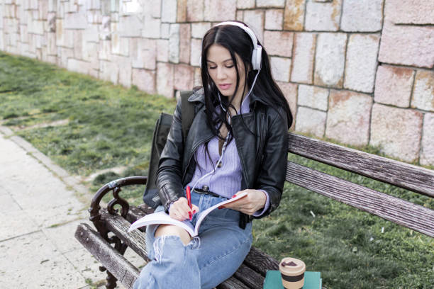 istock Young beautiful female university student with backpack is enjoying near the river. She is wearing headphones and leather jacket while waiting for her college class to start. 2149291222