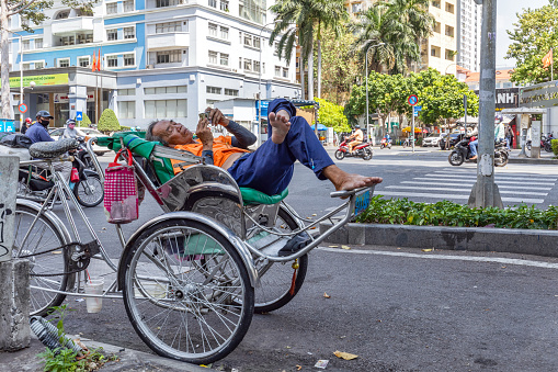 Ho Chi Min, Vietnam - March 11, 2024: Old rickshaw driver rests lying on it and waits for clients