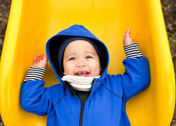 Toddler boy smiling at the bottom of the playground slide.