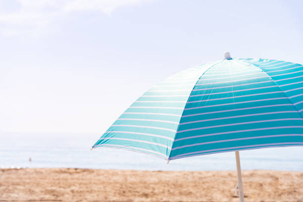 Striped turquoise beach umbrella set in the sand of an uncrowded beach on a beautiful bright morning with copy space. Summer vacation concept