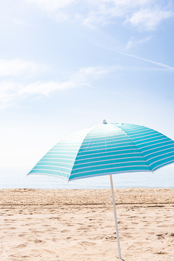 Open turquoise beach umbrella on a deserted beach without people on a beautiful summer morning with copy space. Summer vacation concept