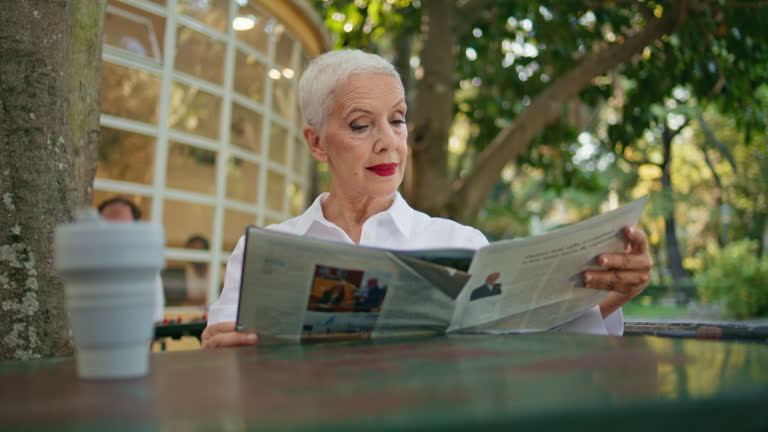 Mature lady looking magazine enjoying summer morning in open air cafe closeup.