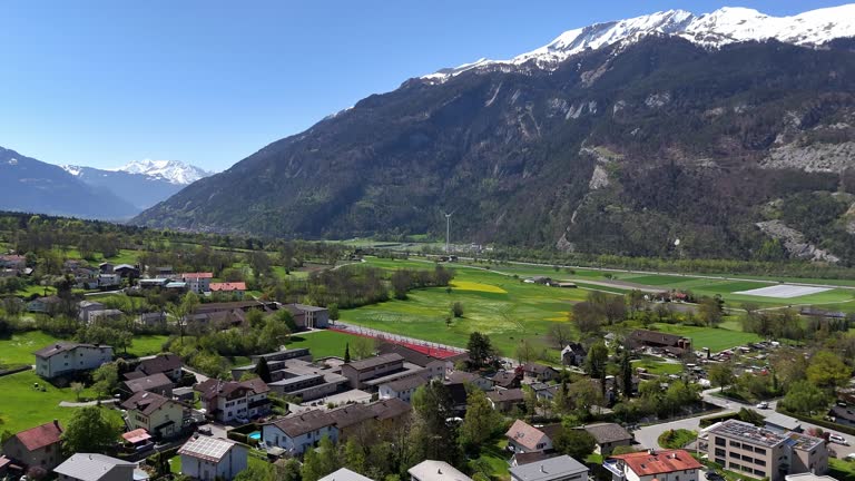 Quaint quiet swiss town of Trimmis with homes and Buildings and alps with snowy peak in background. Drone forward flyover.