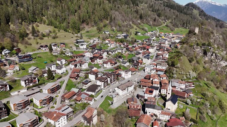 Quaint small town in Switzerland mountain slope during sunny day. Church and historic buildings in city. Aerial top down circling shot.