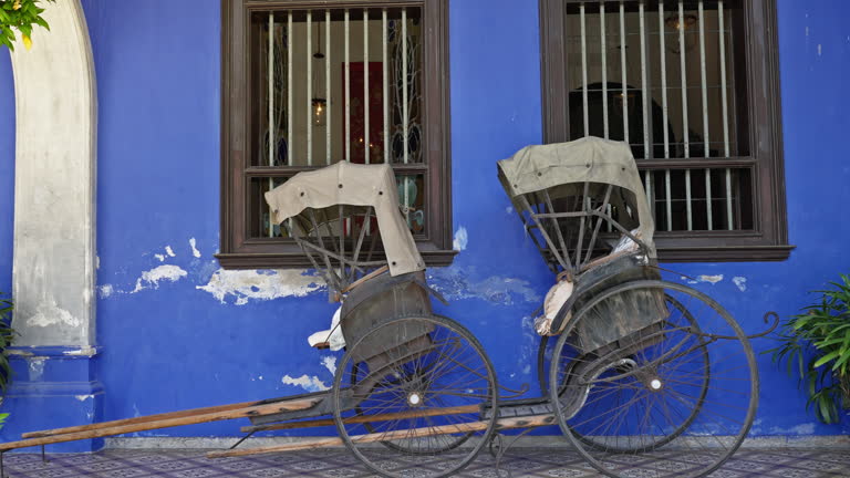 Two traditional hand pulled rickshaws parked together outside of an old colorful blue building in George Town, Malaysia
