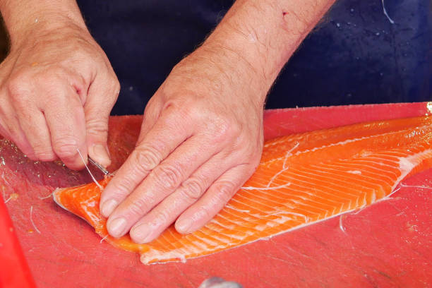 istock Hand cutting salmon on red board in closeup gesture 2149297779