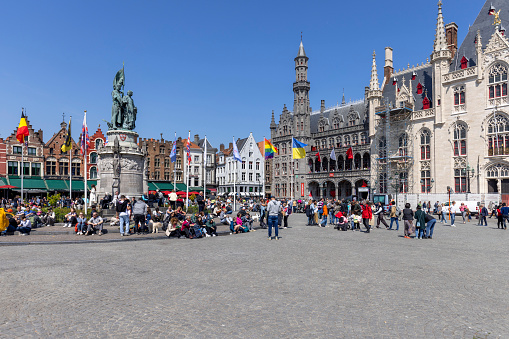 Bruges, Belgium - May 19, 2023: Jan Breydel and Pieter de Coninck Monument on the Market Square (Grote Markt). Colorful traditional tenement houses in the distance