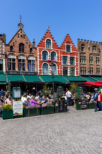 Bruges, Belgium - May 19, 2023: People in front of traditional tenement houses on the Market Square (Grote Markt), outdoor restaurants