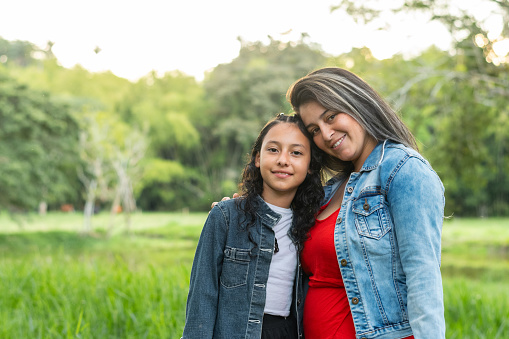 young Latina mother and daughter posing together with a field of green nature in the background.