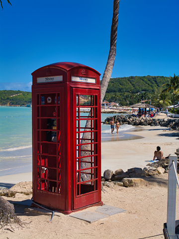 Antigua - Jan 26 2024: A red British phone box at Dickenson Bay in St. Johns, Antigua. Taken on a sunny day with a blue sky.