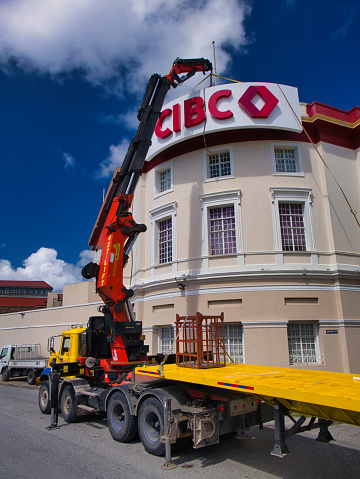 Bridgetown, Barbados - Jan 28 2024: A Palfinger PK 150002 crane lifts a CIBC Caribbean sign from a lorry trailer to be fitted at the top of a building in Bridgetown, Barbados in the Caribbean.