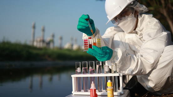 Female scientists wearing Chemical protective suites and PPE collect samples of toxic water to test by mobile lab test, examining wastewater from Industrial, and environment