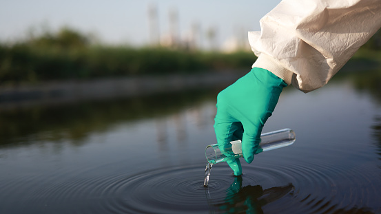 Close-up scientist or environment engineer's hand with a chemical protective suit and PPE collect a sample of toxic wastewater from a chemical flask  from an industrial