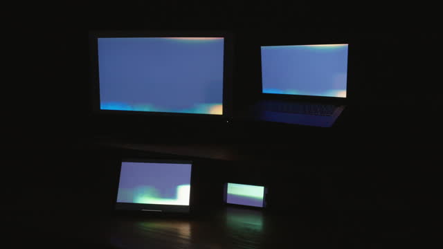 Four digital computer device screens displaying a strobing pattern in a dark room.