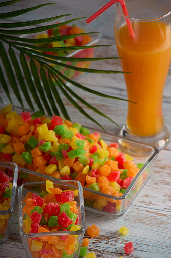 Vertical photo with the image of a glass with delicious freshly squeezed juice standing on the table along with candied fruits in a dish.