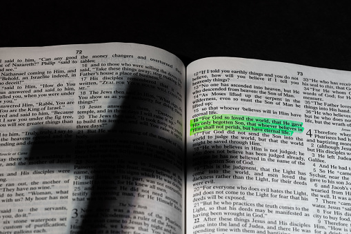 A shadow of a cross on an open bible with highlighted verse.