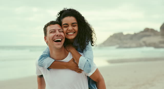 Piggyback, happy and couple at beach on holiday, vacation or travel for romantic date together. Love, smile and young man and woman hugging and having fun by ocean or sea on weekend trip in Mexico.