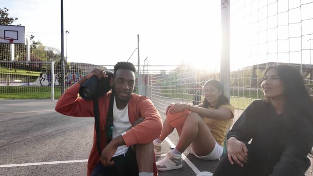 African young man holding radio and singing next to friends in a basketball outdoor urban court