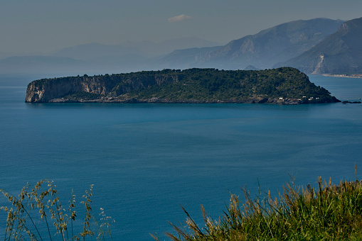 A serene blue water with a rocky island in Cosenza, Calabria, Italia