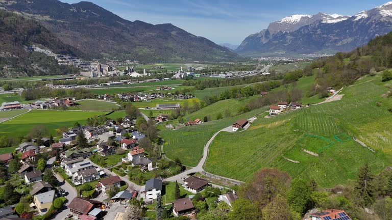Drone flight over apartments in swiss town with solar panels. Cultivation farm fields on hill. Trimmis, Switzerland.