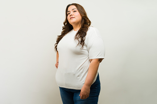 T-shirt mockup of a confident curvy plus-size woman striking a pose against a studio backdrop