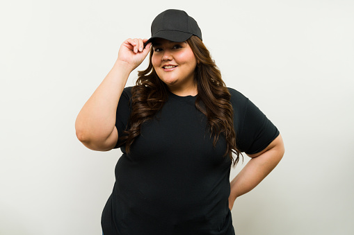 Smiling plus-size woman in a black t-shirt and cap posing confidently in a studio setting for a mockup