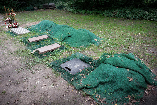 several urn graves lined with green mats and provided with protective lids in advance of a burial in a cemetery for the poor