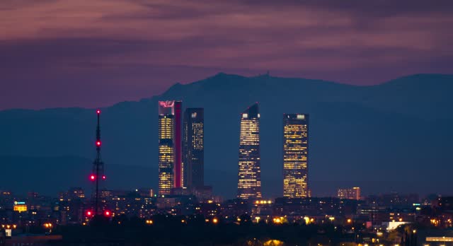 Timelapse of Madrid skyline with 5 towers business area CTBA and snowy Sierra mountain peaks as background sunset day to night time-lapse