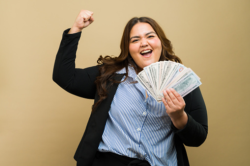 Happy plus-size woman beaming and holding money, rejoicing in her financial success in a professional studio environment