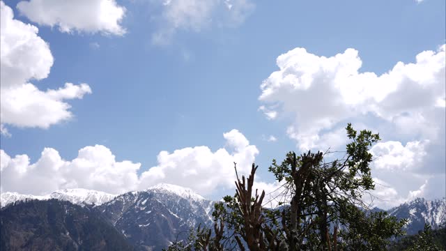 Timelapse of Snow-capped mountains with fluffy clouds overhead dissolving in the sky