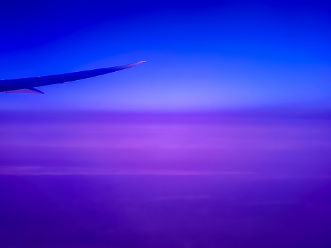 Plane flying high above cloud layer viewed through the Electronically Dimmable (Electrochromic) window. Features the blue and violet stratosphere and slight curvature of the Earth.