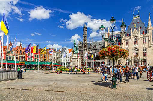 Bruges, Belgium, July 5, 2023: people tourists on Market square, colorful Flemish style buildings, Provincial Court, Historium Bruges museum in Brugge old town historical city centre