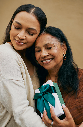 A daughter embraces her mother in a warm hug, while presenting her with a thoughtful gift, be it for Mother's Day or her birthday.