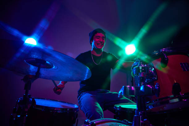 istock Overjoyed stylish drummer performing in pink-purple stage lighting against gradient studio background. 2149327239
