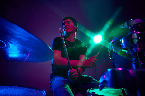 istock Musician enjoying drum session in pink-purple stage lighting against gradient studio background. 2149327242