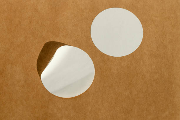 istock Round white stickers on brown paper background with natural sunlight. 2149327358
