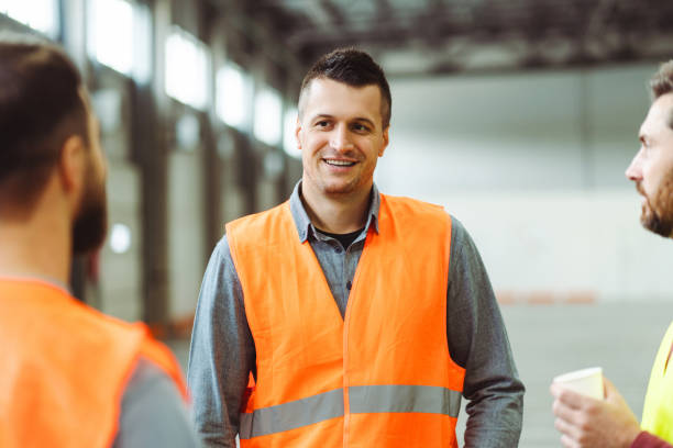 istock Attractive, smiling man, foreman wearing workwear, talking with colleagues, standing in warehouse 2149327502
