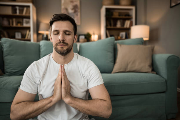 Tranquil young man doing yoga and meditating at home.