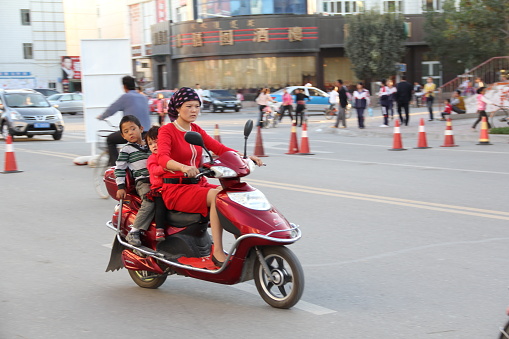 Urumqi, Xinjiang, China - 09/20/2011: A Chinese woman driving a scooter and her two children riding behind her.