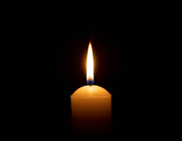 istock A single burning candle flame or light glowing on a big yellow candle on black or dark background on table in church for Christmas, funeral or memorial service with copy space 2149334917