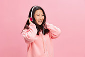 Smiling cutie cute Asian young lady in pink hoodie sweatshirt with cute headphones looks at you with love posing isolated on pink studio background. Good offer. Sound streaming platform ad concept