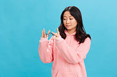 Focused cute Asian student young lady in pink hoodie sweatshirt ready to wear round glasses posing isolated on over blue studio background. The best offer for ad. Eyewear for vision correction concept