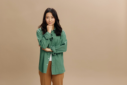 Upset frustrated Asian student young woman in khaki green shirt crossing hands posing isolated on over beige pastel studio background. Cool fashion offer. Lifestyle and Emotions concept