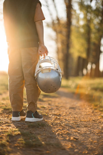 Low section shot of unrecognizable boy standing and holding rugby helmet in nature at sunset