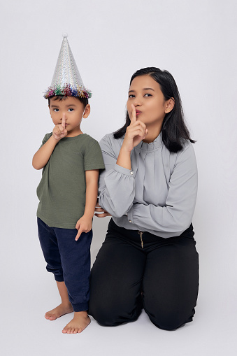 Full body smiling happy mother and kid boy asian wearing casual clothes and silver cone hat showing silent gesture isolated on white background