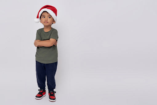 Smiling happy child Asian kid boy wearing casual clothes Christmas hat standing confident with crossed arms and celebrating Christmas isolated on white background