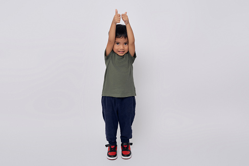Full body little small smiling happy Asian boy 2-3 years old wearing green t-shirt standing confident while showing thumbs up like gesture isolated on white background
