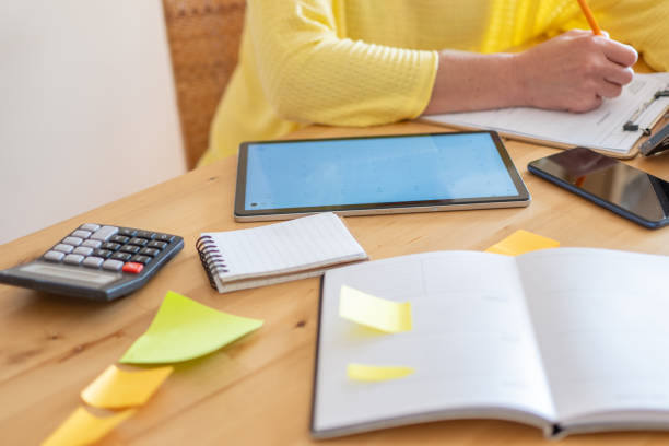 Self-Sufficient Woman Filling Out Documents In Her Workspace, Uses Technology And Office Supplies, Works From Home.